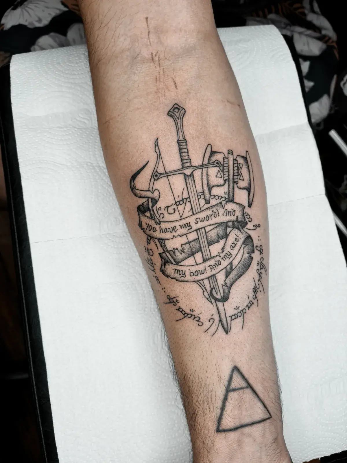 Tatuagem geek de O Senhor dos Anéis com espada, arco e machado e a frase You have my sword, no antebraço
