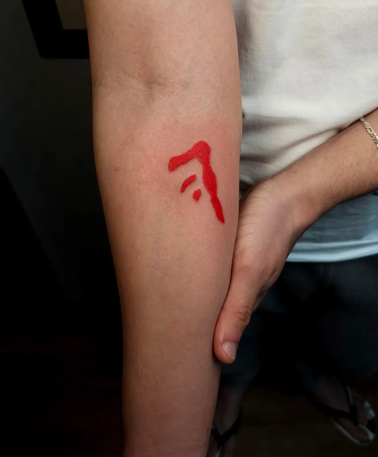 Tatuagem geek de Supernatural com a Marca de Caim em vermelho sólido no antebraço