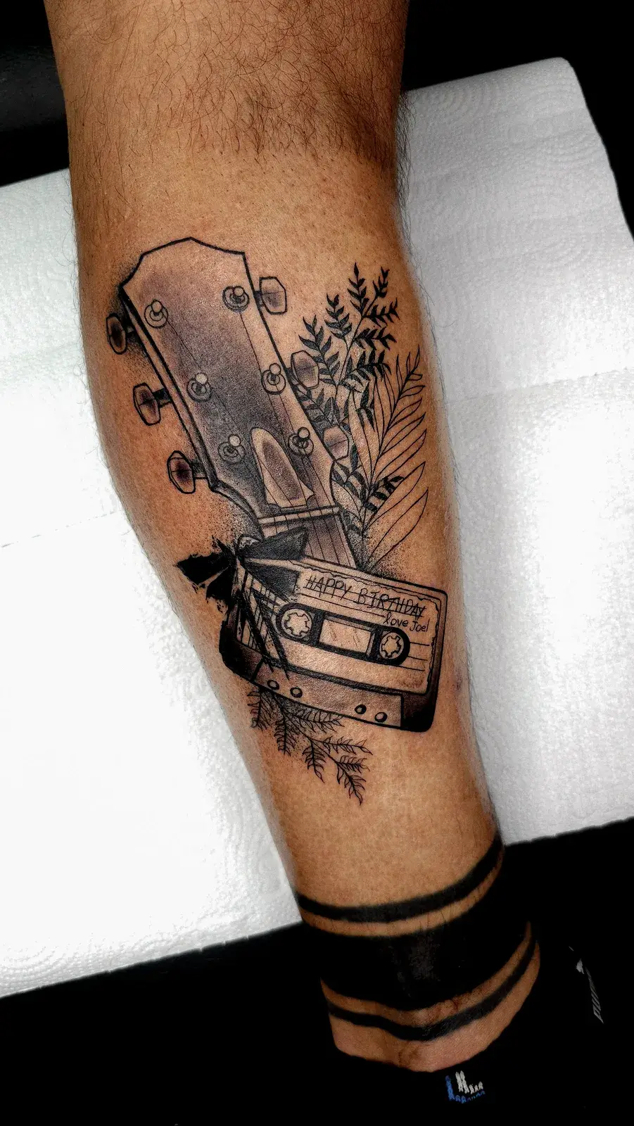 Tatuagem geek de The Last of Us com braço de violão e fita cassete, em blackwork na panturrilha